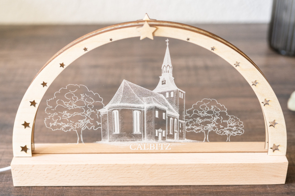 LED-Schwibbogen aus Holz mit Sternmotiven und gravierter Calbitzer Kirche auf Acrylplatte, warmweiß beleuchtet.
